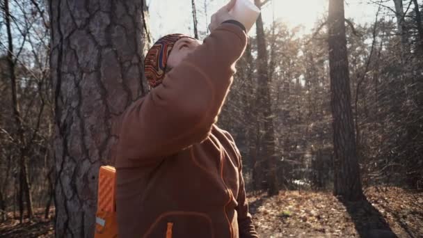 Un jeune homme caucasien fatigué fait une pause avec un sac à dos assis et de l'eau potable sur un arbre dans une forêt naturelle lors de randonnées, voyages, vacances, en vacances, concept de liberté de style de vie en plein air 
