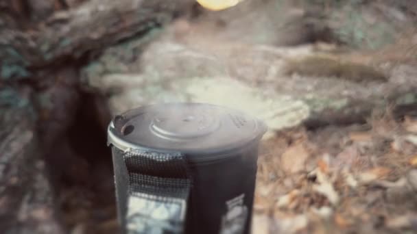 Primer plano de un quemador de gas, en el que se encuentra una tetera con tapa, hierve agua, vapor, cocina en condiciones al aire libre. Hierve la comida. En la orilla del río en el bosque. 4K — Vídeo de stock