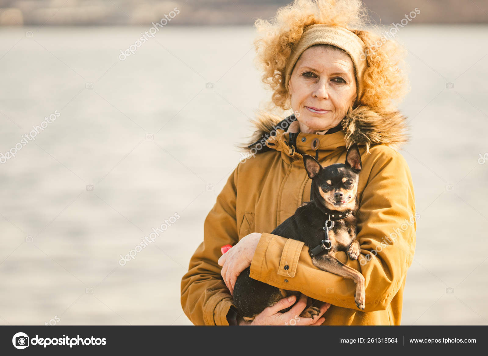 Portrait of an adult blonde curly hair Caucasian woman holding a small black-colored dog breed Portrait of an adult blonde curly hair Caucasian woman holding a small black-colored dog breed