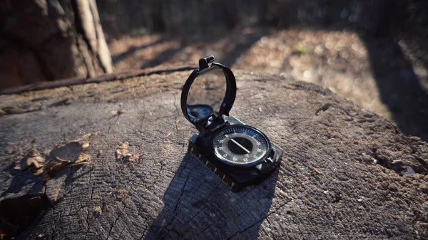 Tématem je turistika a technika. Prosluněný navigační kompas s černou magnetickou jehlou ležící na pahýlu v lese za slunečného počasí — Stock fotografie