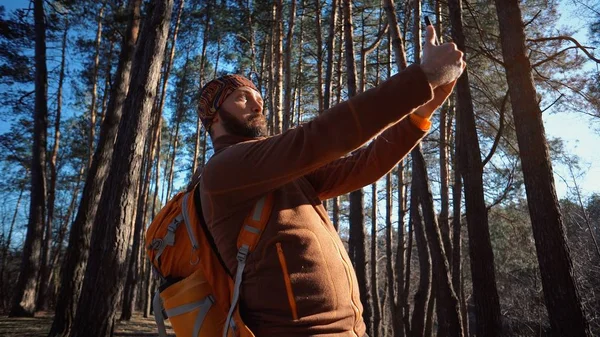 Przystojny kaukaski Hiker zrobić zdjęcie selfie. Backpacker z szczęśliwym uśmiechem trzyma smartfon w lesie. Szczęśliwy uśmiechnięty turysta Wędrowiec turystyka z plecak robi a zabawny twarz — Zdjęcie stockowe