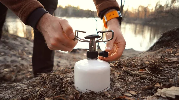 Elleri beyaz erkek gezgin, turist göl kamp yakınındaki ormanda oturur. Yemek pişirmek için envanter kullanır. Bir el çakmağı gaz balonuyla meşaleyi ateşe verdi