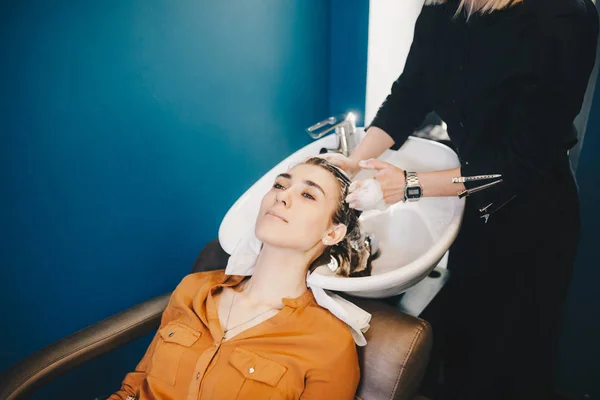 Beleza, cuidado do cabelo e conceito de pessoas - mulher jovem feliz com cabeleireiro cabeça de lavagem no salão de cabeleireiro — Fotografia de Stock