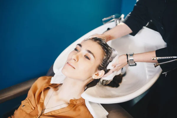 Beleza, cuidado do cabelo e conceito de pessoas - mulher jovem feliz com cabeleireiro cabeça de lavagem no salão de cabeleireiro — Fotografia de Stock