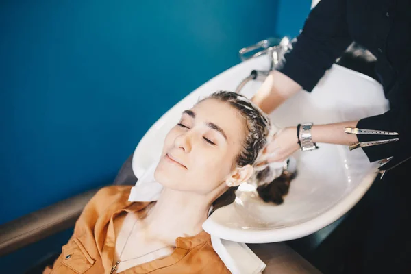 Beleza, cuidado do cabelo e conceito de pessoas - mulher jovem feliz com cabeleireiro cabeça de lavagem no salão de cabeleireiro — Fotografia de Stock