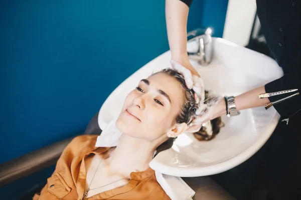 Красота, уход за волосами и концепция людей - счастливая молодая женщина с парикмахерской моет голову в парикмахерской — стоковое фото