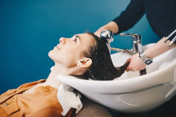 Beleza, cuidado do cabelo e conceito de pessoas - mulher jovem feliz com cabeleireiro cabeça de lavagem no salão de cabeleireiro — Fotografia de Stock