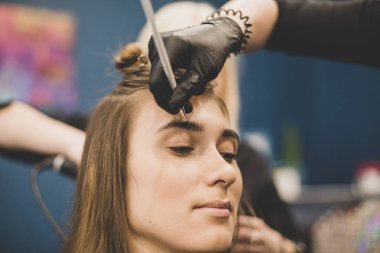 Kaş boyama işi. Usta, güzel bir kıza kına ile kaşlarını boyuyor, bir güzellik uzmanının salonunda fırçayla boya yapıyor. Kaş mimarisi