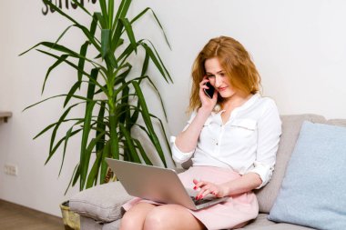 Mutlu kadın dizüstü bilgisayar ile kanepede oturan ve evde telefonda konuşurken. Genç başarılı iş kadını telefonda konuşurken evden çalışıyor. Dizüstü bilgisayarda okuyan ve telefon kullanan üniversite öğrencisi