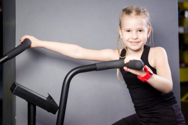 Spor salonunda egzersiz bisikleti kullanan küçük çekici beyaz çocuk. Fitness. Crossfit spor salonunda kardiyo egzersiz için bir hava bisikleti kullanan küçük bir atlet. Bisiklet makinesinde oturan spor kız