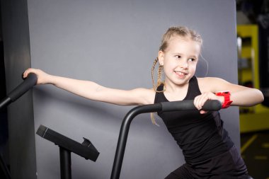 Spor salonunda egzersiz bisikleti kullanan küçük çekici beyaz çocuk. Fitness. Crossfit spor salonunda kardiyo egzersiz için bir hava bisikleti kullanan küçük bir atlet. Bisiklet makinesinde oturan spor kız