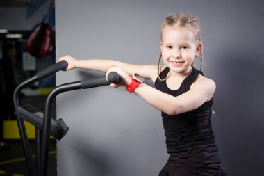Spor salonunda egzersiz bisikleti kullanan küçük çekici beyaz çocuk. Fitness. Crossfit spor salonunda kardiyo egzersiz için bir hava bisikleti kullanan küçük bir atlet. Bisiklet makinesinde oturan spor kız