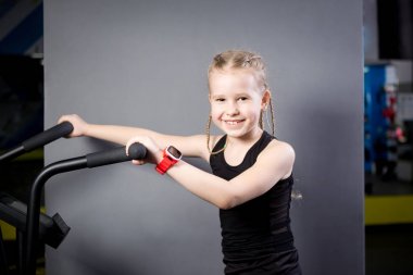 Spor salonunda egzersiz bisikleti kullanan küçük çekici beyaz çocuk. Fitness. Crossfit spor salonunda kardiyo egzersiz için bir hava bisikleti kullanan küçük bir atlet. Bisiklet makinesinde oturan spor kız