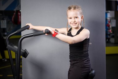 Spor salonunda egzersiz bisikleti kullanan küçük çekici beyaz çocuk. Fitness. Crossfit spor salonunda kardiyo egzersiz için bir hava bisikleti kullanan küçük bir atlet. Bisiklet makinesinde oturan spor kız