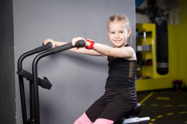 Spor salonunda egzersiz bisikleti kullanan küçük çekici beyaz çocuk. Fitness. Crossfit spor salonunda kardiyo egzersiz için bir hava bisikleti kullanan küçük bir atlet. Bisiklet makinesinde oturan spor kız