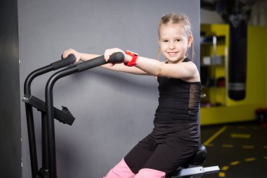 Spor salonunda egzersiz bisikleti kullanan küçük çekici beyaz çocuk. Fitness. Crossfit spor salonunda kardiyo egzersiz için bir hava bisikleti kullanan küçük bir atlet. Bisiklet makinesinde oturan spor kız