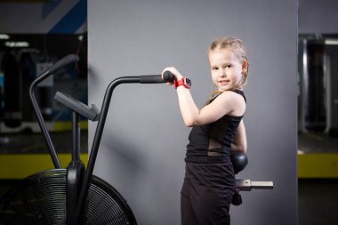 Spor salonunda egzersiz bisikleti kullanan küçük çekici beyaz çocuk. Fitness. Crossfit spor salonunda kardiyo egzersiz için bir hava bisikleti kullanan küçük bir atlet. Bisiklet makinesinde oturan spor kız
