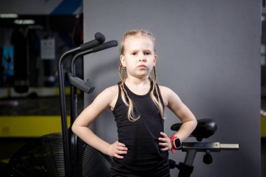 Spor salonunda egzersiz bisikleti kullanan küçük çekici beyaz çocuk. Fitness. Crossfit spor salonunda kardiyo egzersiz için bir hava bisikleti kullanan küçük bir atlet. Bisiklet makinesi yakınında poz atletik kız