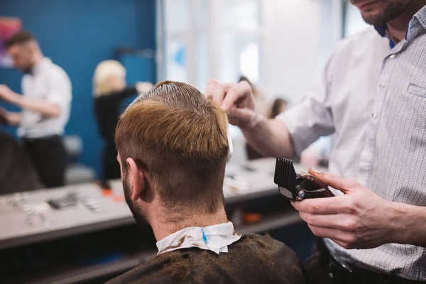 Close up shot of man getting trendy haircut at barber shop. Male hairstylist serving client, making haircut using machine and comb — Stock Photo, Image