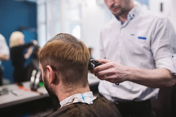 Close up shot of man getting trendy haircut at barber shop. Male hairstylist serving client, making haircut using machine and comb — Stock Photo, Image