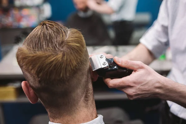 Tiro de perto de um homem a cortar o cabelo na barbearia. Cabeleireiro masculino servindo cliente, fazendo corte de cabelo usando máquina e pente — Fotografia de Stock
