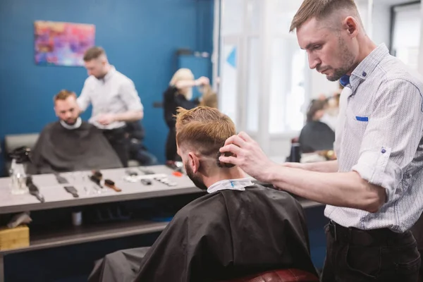 Close up shot of man getting trendy haircut at barber shop. Male hairstylist serving client, making haircut using machine and comb — Stock Photo, Image