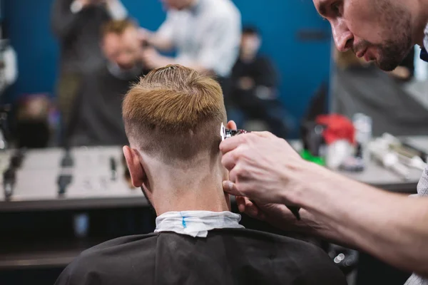 Close up shot of man getting trendy haircut at barber shop. Male hairstylist serving client, making haircut using machine and comb — Stock Photo, Image