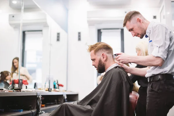 Крупный план человека, стригущегося в парикмахерской. Мужчина парикмахер, обслуживающий клиента, делает стрижку с помощью машины и расчески — стоковое фото