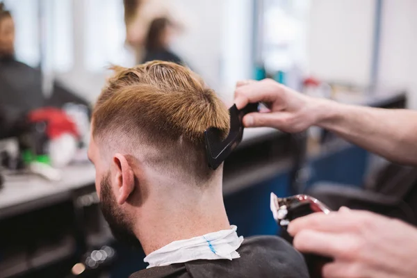 Close up shot of man getting trendy haircut at barber shop. Male hairstylist serving client, making haircut using machine and comb — Stock Photo, Image