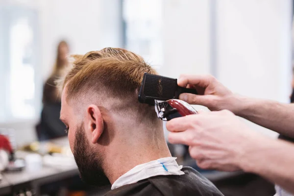 Close up shot of man getting trendy haircut at barber shop. Male hairstylist serving client, making haircut using machine and comb — Stock Photo, Image