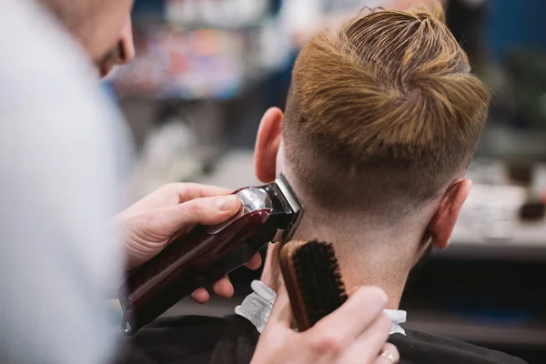 Nära upp skott av mannen få trendiga frisyr på frisör. Manlig Frisör servering kund som gör frisyr med machine och kam — Stockfoto