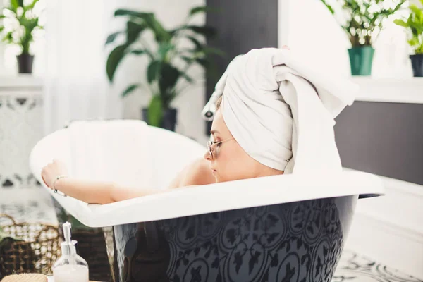 Mujer joven caucásica con toalla en la cabeza y gafas de sol recibiendo tratamiento de spa en un salón de belleza, dentro de una habitación interior. Relajante en el baño en ropa de cama. El concepto de cuidado corporal y relajación — Foto de Stock