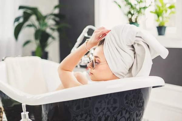 Young caucasian woman with towel on head and sunglasses getting spa treatment in a beauty salon, inside an interior room. Relaxing in the bathroom in linen. The concept of body care and relaxation — Stock Photo, Image