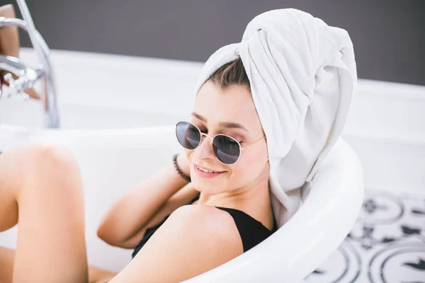 Young caucasian woman with towel on head and sunglasses getting spa treatment in a beauty salon, inside an interior room. Relaxing in the bathroom in linen. The concept of body care and relaxation — Stock Photo, Image