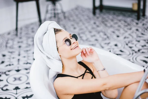 Young caucasian woman with towel on head and sunglasses getting spa treatment in a beauty salon, inside an interior room. Relaxing in the bathroom in linen. The concept of body care and relaxation — Stock Photo, Image