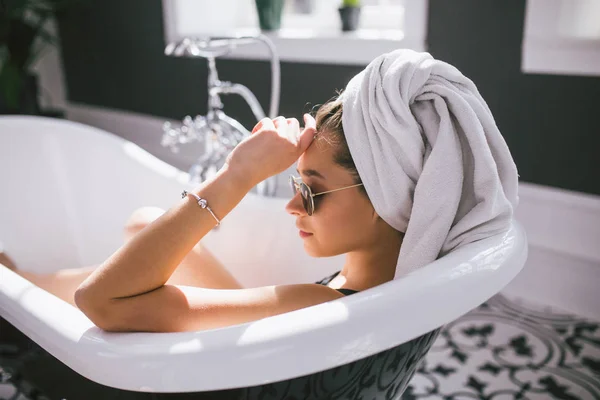 Jeune femme caucasienne avec serviette sur la tête et lunettes de soleil obtenir un traitement spa dans un salon de beauté, à l'intérieur d'une pièce intérieure. Détente dans la salle de bain en lin. Le concept de soin du corps et de relaxation — Photo