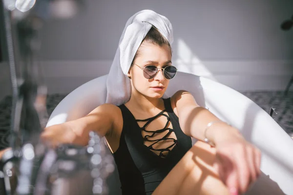 Mujer joven caucásica con toalla en la cabeza y gafas de sol recibiendo tratamiento de spa en un salón de belleza, dentro de una habitación interior. Relajante en el baño en ropa de cama. El concepto de cuidado corporal y relajación —  Fotos de Stock