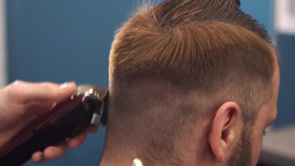 Un primo piano di un uomo che si fa tagliare i capelli alla moda dal barbiere. Maschio parrucchiere servire cliente, rendendo taglio di capelli utilizzando macchina e pettine — Video Stock