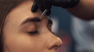 Kaş boyama işi. Usta, güzel bir kıza kına ile kaşlarını boyuyor, bir güzellik uzmanının salonunda fırçayla boya yapıyor. Kaş mimarisi