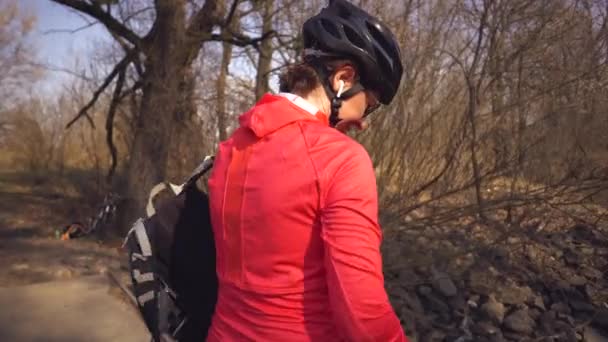 Vrolijke blanke vrouw fietser maakt een foto van zichzelf een selfie aan de telefoon tijdens het zitten op de brug over een rivier in het bos bij zonnig weer — Stockvideo