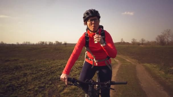 Atletische blanke vrouw eet eiwit Barrit op mountainbike op de natuur. Jonge sportieve vrouw atleet in helm rusten terwijl bijten voeding bar. Fitness vrouw eten energie snack buiten — Stockvideo