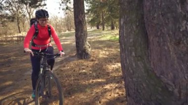 Tema spor ve doğada turizm. Ormanda dağ bisikletine binen kasklı ve spor giyimli beyaz genç kadın bisikletçi. Dinlenmek ve ağacın altında su içmek ve şişeler içmek durdurmak