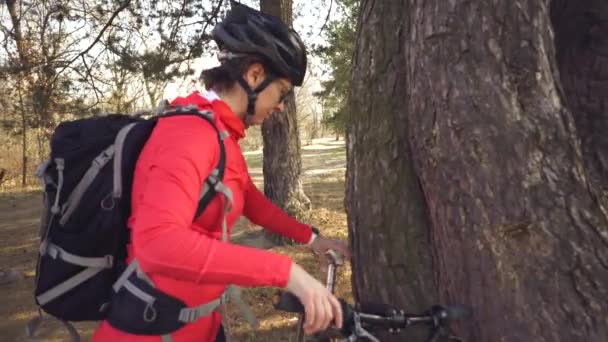 Deportes temáticos y turismo en la naturaleza. Joven ciclista caucásica con casco y ropa deportiva montada en una bicicleta de montaña en el bosque. Deténgase para descansar y beber agua, beber y frascos bajo el árbol — Vídeo de stock