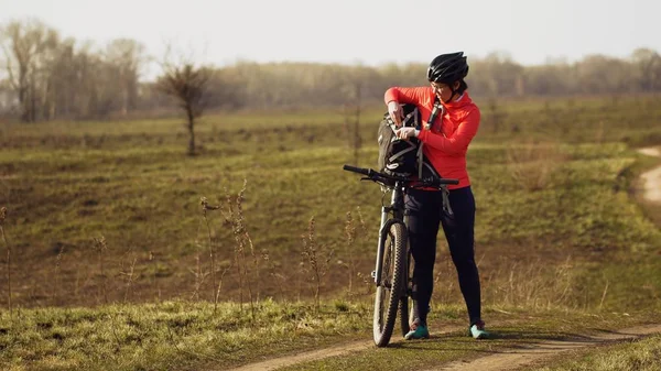 Athletic kaukaski kobieta zjada białka bar jeździć na rowerze górskim na naturę. Młoda sportowa kobieta sportowiec w kasku odpoczynku podczas gryzienia odżywcze bar. Fitness kobieta jedzenia energii przekąskę na zewnątrz — Zdjęcie stockowe