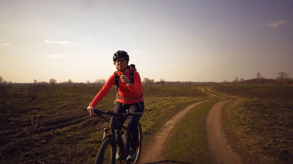 Athletic kaukaski kobieta zjada białka bar jeździć na rowerze górskim na naturę. Młoda sportowa kobieta sportowiec w kasku odpoczynku podczas gryzienia odżywcze bar. Fitness kobieta jedzenia energii przekąskę na zewnątrz — Zdjęcie stockowe
