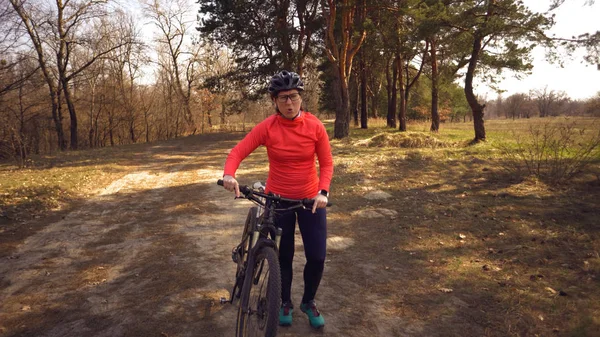 The topic health problems with athletes. Caucasian woman cyclist on mountain bike finish workout in forest. Emotion tired, hard fast heart beating and hard to breathe. Cardiac pathology tachycardia