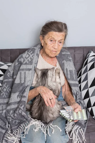 Tema vecchiaia, solitudine assistenza sanitaria. vecchia donna caucasica dai capelli grigi con rughe profonde seduta con gatto animale domestico. povera nonna in possesso di farmaci pillola blister. L'emozione dispera paura e dolore — Foto Stock