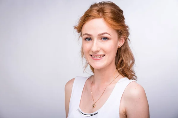 Retrato de una hermosa joven estudiante con una sonrisa en una camisa blanca de nacionalidad europea, caucásica con el pelo largo y rojo y pecas en su cara posando sobre un fondo blanco en el estudio — Foto de Stock