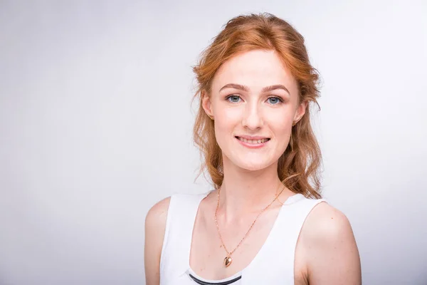 Retrato de una hermosa joven estudiante con una sonrisa en una camisa blanca de nacionalidad europea, caucásica con el pelo largo y rojo y pecas en su cara posando sobre un fondo blanco en el estudio — Foto de Stock