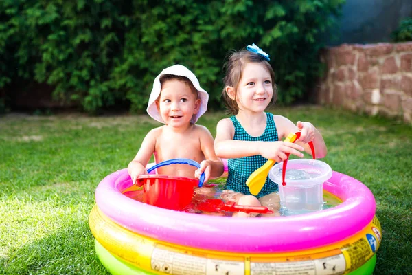 Thema Kindersommerspiele im Hof. Kaukasisches Geschwisterpaar spielt Plastik-Spielzeug-Eimer im Wasser, aufblasbares rundes Kinderbecken. Sommer ist heiß, Ruhe in Badeanzügen — Stockfoto